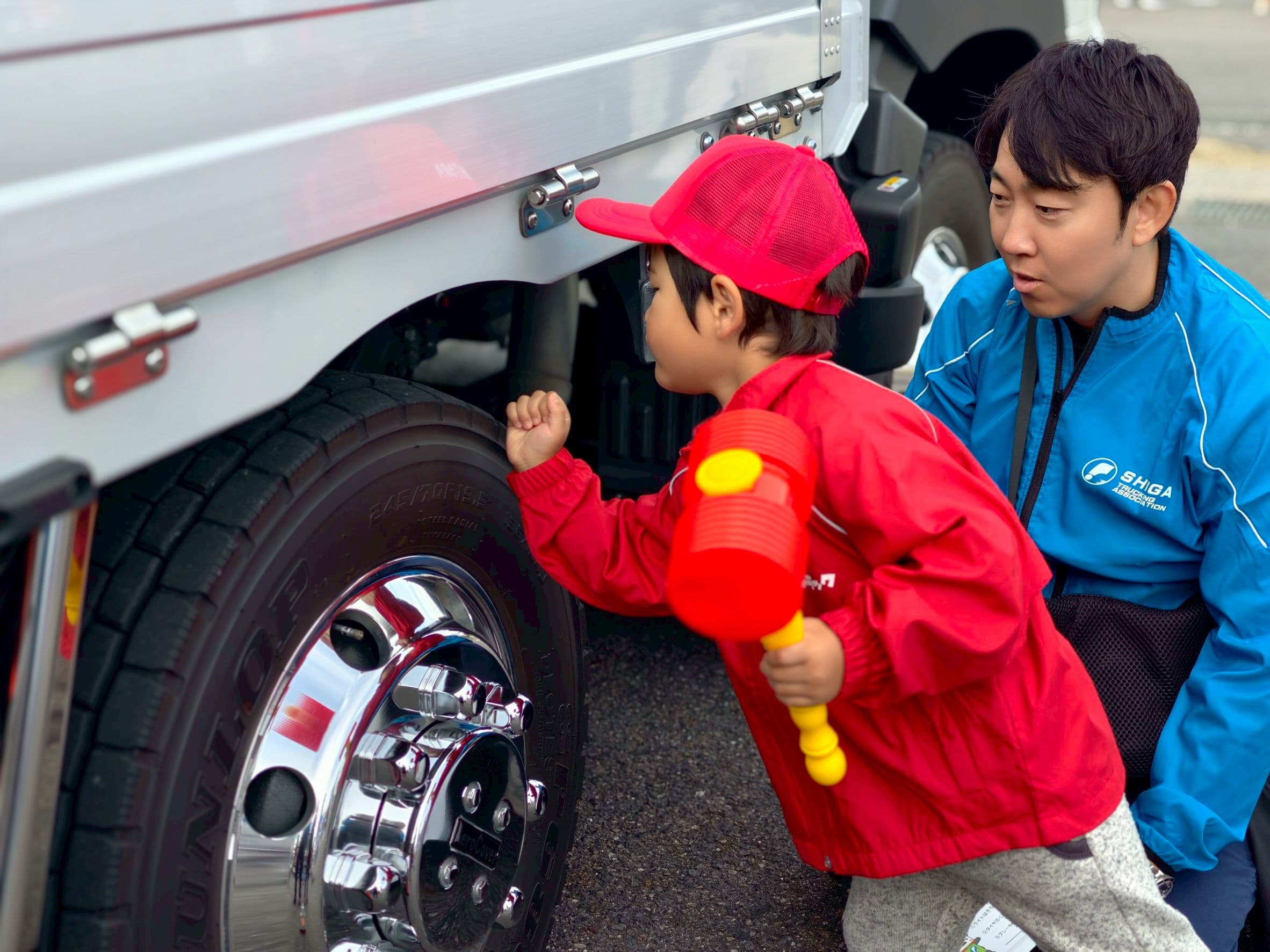 トラックのタイヤを点検ハンマーでたたいて確かめる子ども