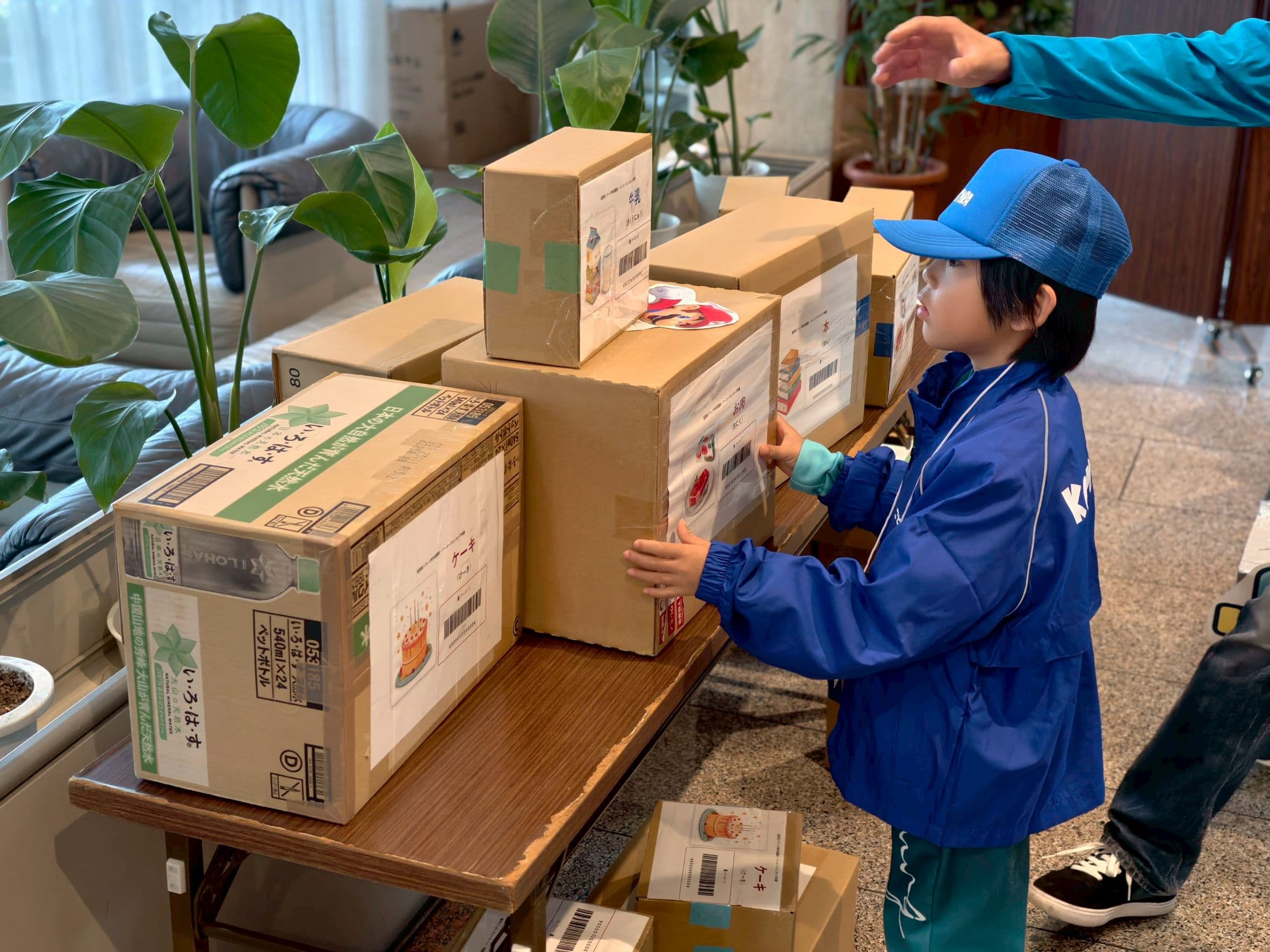 牛乳やケーキなどの荷物をバーコードで確認しながら集める子ども