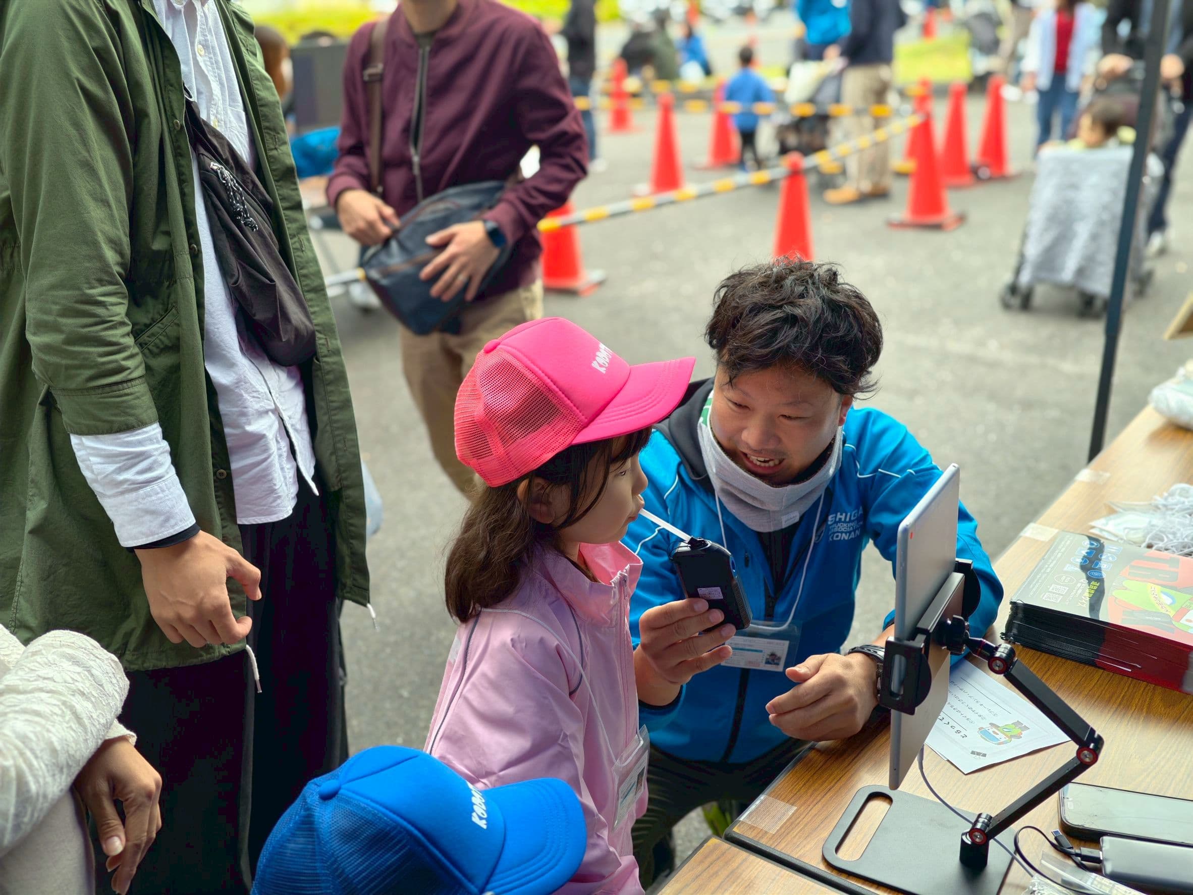 アルコールチェッカーに息を吹きこんで点呼を受ける子ども